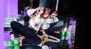 comédienne assise par terre, criant, avec ses baskets rouge aux pieds