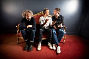 Trois musiciens assis sur un canapé se disputant pour de faux