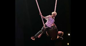 une femme et un homme se font face, suspendus dans les airs, sur une corde